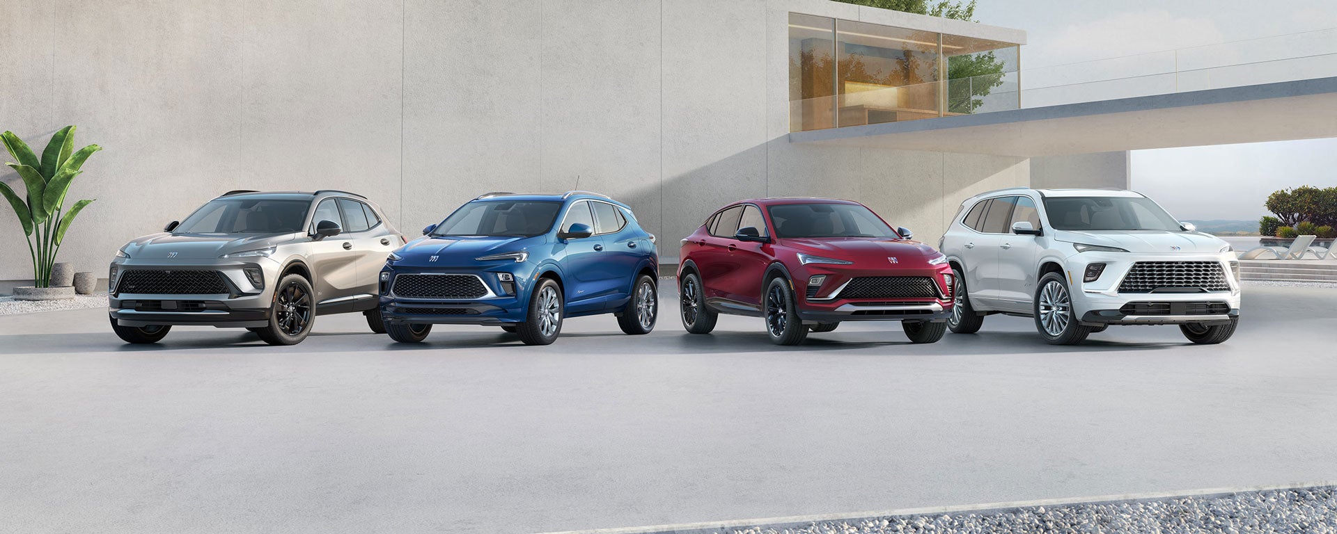 Four new Buick SUVs in light grey, blue, maroon, and white parked in a row outside a modern building.