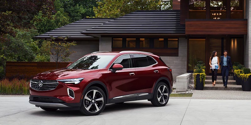 Red Buick SUV parked in the driveway of a modern home with two people walking near the entrance