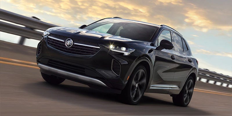 Black Buick SUV driving on a highway at sunset with a bridge guardrail in the background