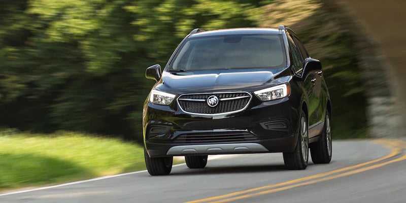 Black Buick SUV driving on a winding road surrounded by lush green trees