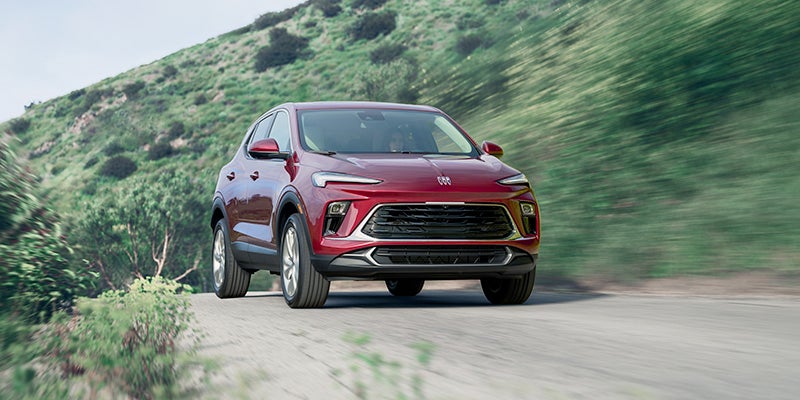 Red Buick SUV in motion on a winding road with grassy hills in the background, highlighting the vehicle's front grille and exterior styling