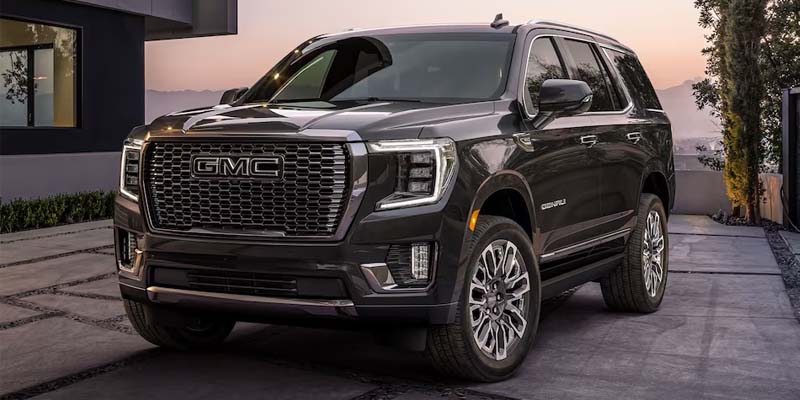 Black GMC Yukon SUV parked in a residential driveway, showcasing its chrome grille and premium exterior design