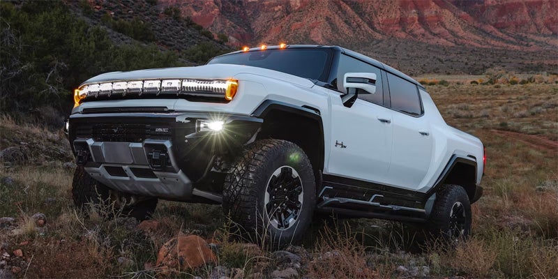 White GMC HUMMER EV Pickup navigating rugged off-road terrain with mountains in the background