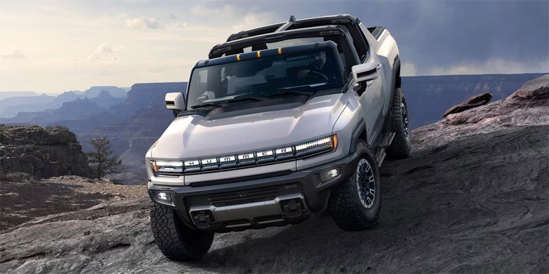 Silver GMC Hummer EV pickup truck driving on a steep rocky off-road trail in a canyon landscape