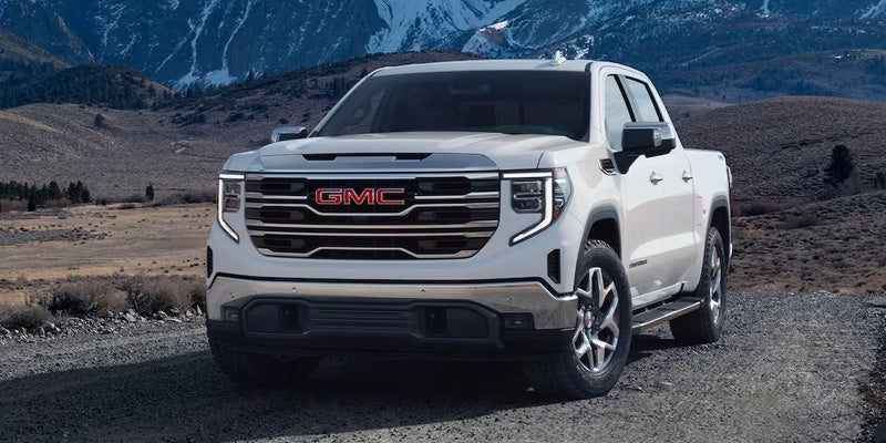 White GMC Sierra pickup truck parked on a gravel road with mountains in the background