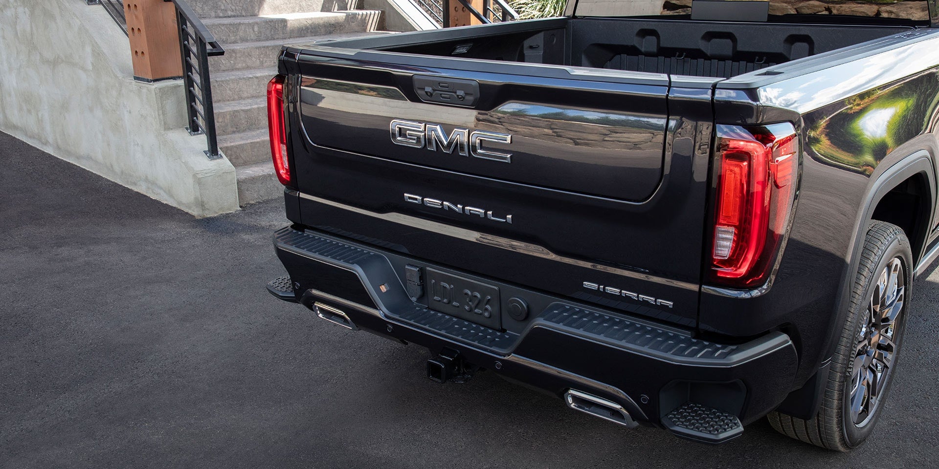 Rear view of a black GMC Sierra Denali pickup truck showing the tailgate, LED taillights, and integrated step bumper