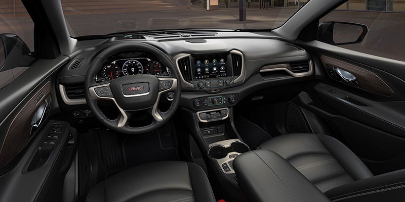 Front interior view of a GMC vehicle featuring a leather-wrapped steering wheel, digital instrument cluster, touchscreen infotainment system, and black leather seats