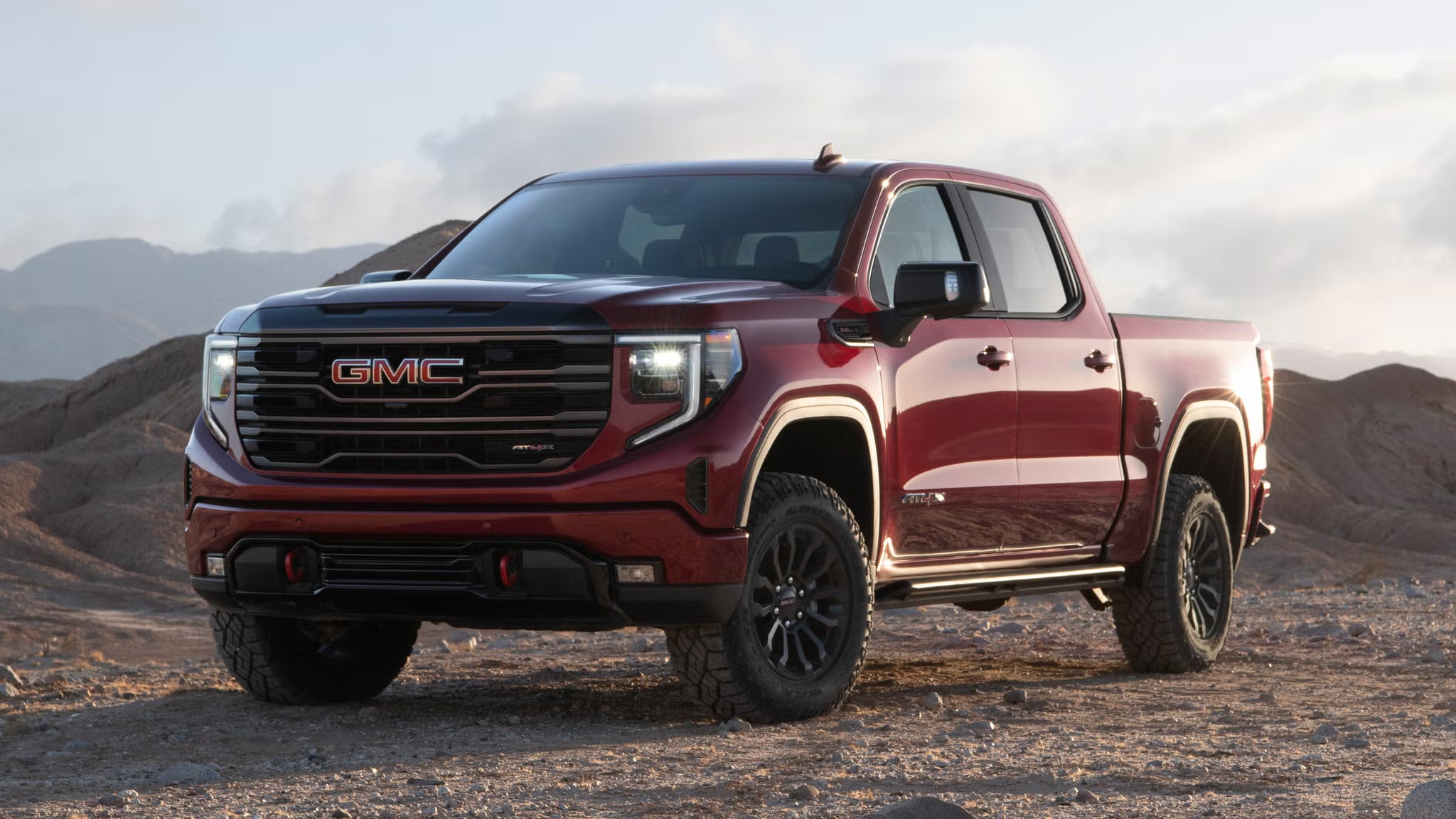Red GMC Sierra pickup truck parked on a rugged desert landscape with mountains in the background