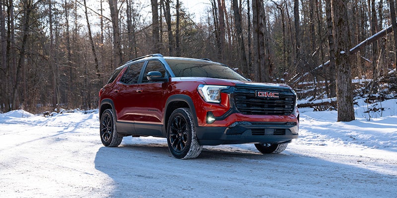 Red GMC Terrain SUV driving on a snow-covered road through a winter forest landscape