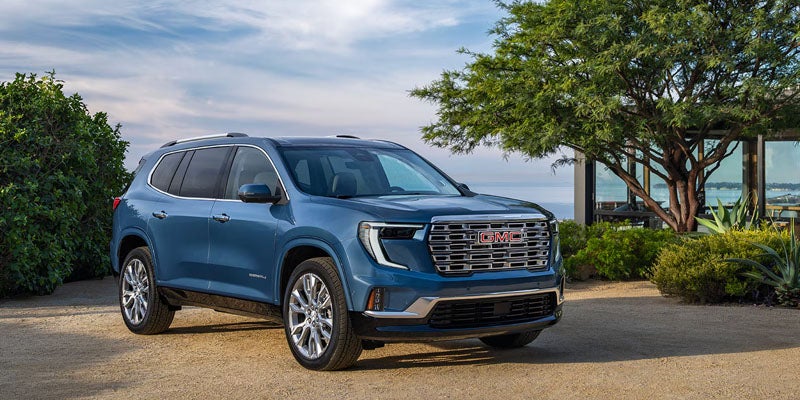 Blue GMC SUV parked on a paved driveway near landscaped greenery, shown from a front three-quarter angle