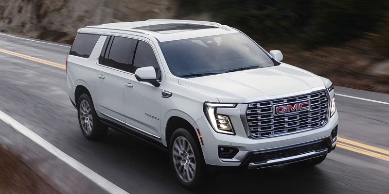 White GMC Yukon XL SUV driving on a highway, viewed from an elevated front three-quarter angle