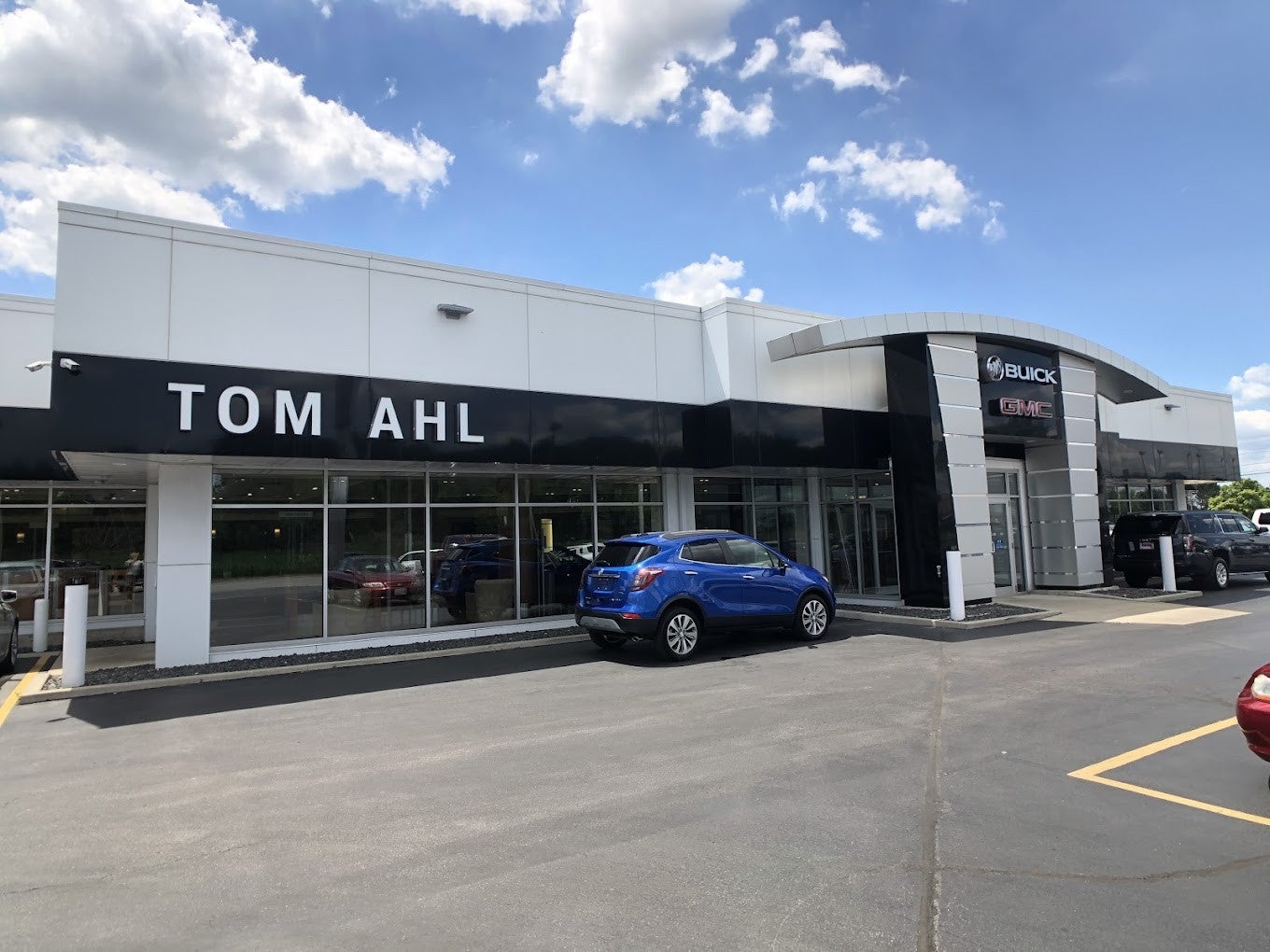 Exterior view of Tom Ahl Buick GMC dealership building with a blue SUV parked in front under a partly cloudy sky.