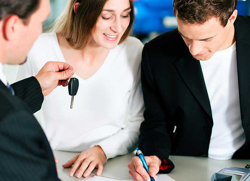 Car buyer completing paperwork and accepting vehicle keys at dealership