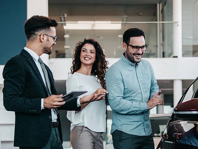 Customers consulting with an auto sales representative at a dealership