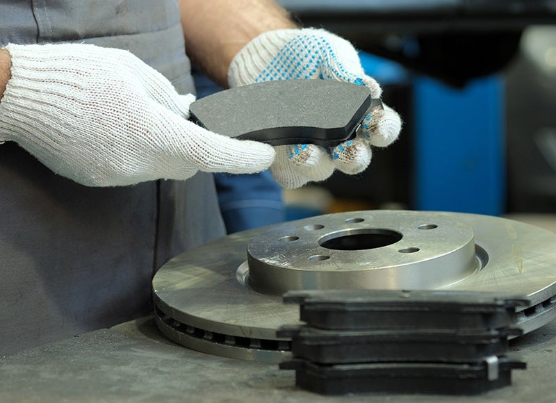 Close-up of a technician wearing work gloves holding a brake pad above a brake rotor on a workbench