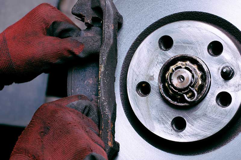 Mechanic's gloved hands working on a brake pad next to a brake rotor during a vehicle brake service