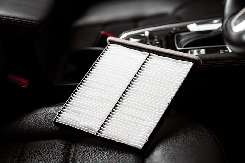 Clean white cabin air filter resting on a black vehicle seat, with part of the center console visible in the background