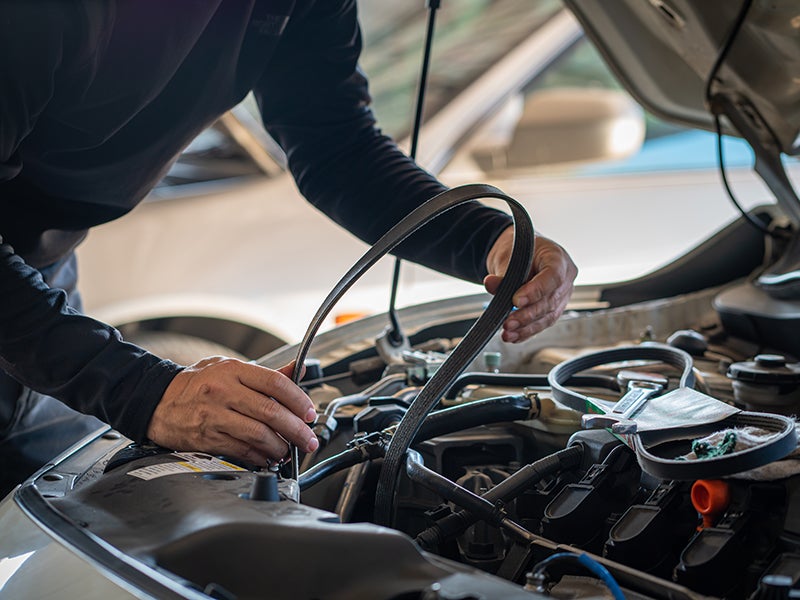 Technician inspecting and servicing a vehicle engine compartment with diagnostic equipment during routine maintenance