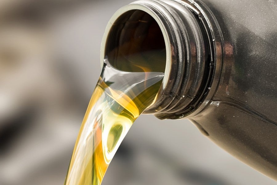 Close-up of golden motor oil being poured from a plastic container, with oil flowing smoothly from the bottle opening against a blurred background