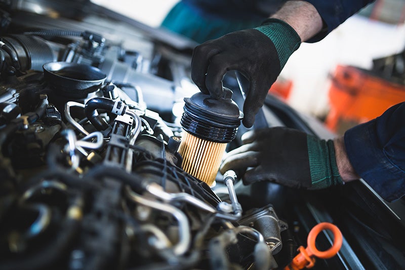 Technician replacing an engine oil filter during vehicle maintenance under an open hood