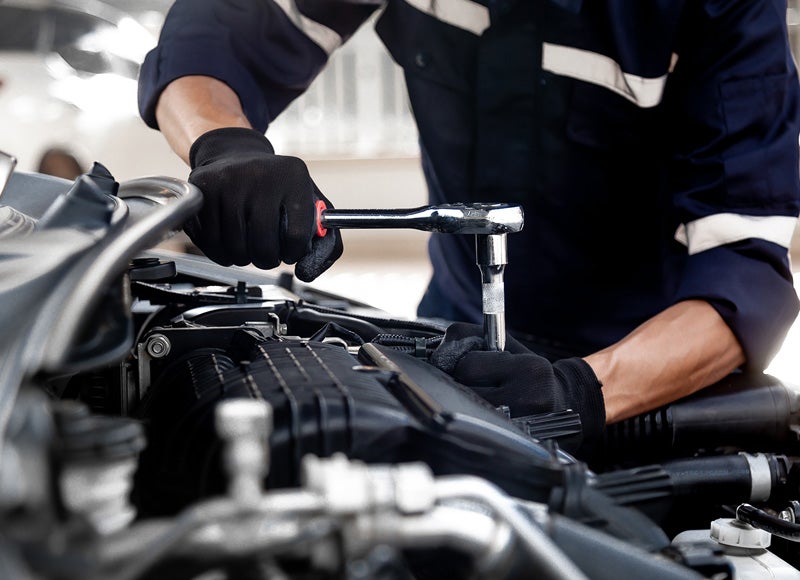 Technician using a socket wrench to perform maintenance on a vehicle engine under an open hood