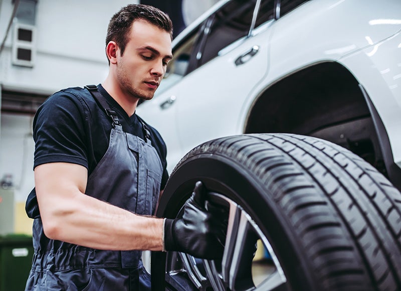 Automotive technician installing or inspecting a tire on a white SUV in a vehicle service center